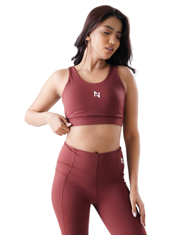 Woman wearing a maroon sports bra and leggings with a logo on a white background