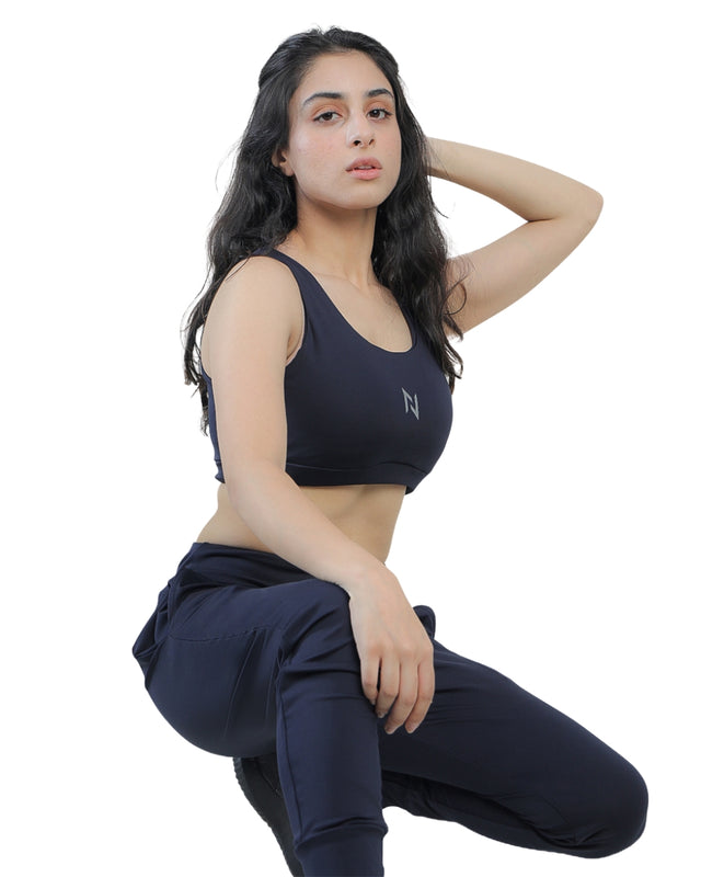 Woman wearing a black sports bra and navy pants on a white background
