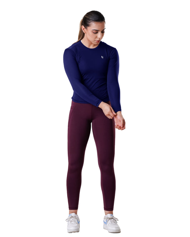 Woman wearing a navy long-sleeve top and maroon leggings on a white background