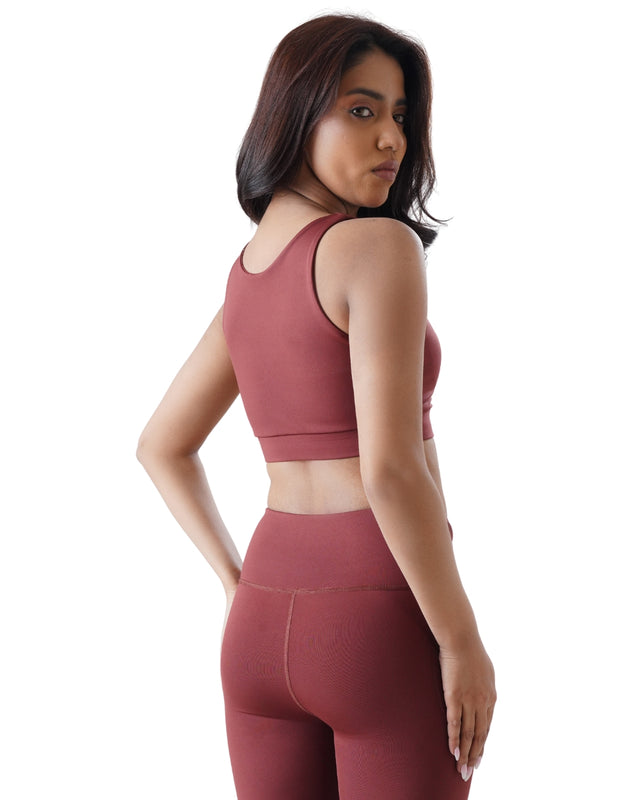 Woman wearing a maroon sports bra and leggings on a white background