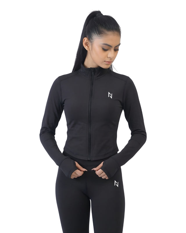 Woman wearing a black athletic jacket and leggings with a logo on a white background