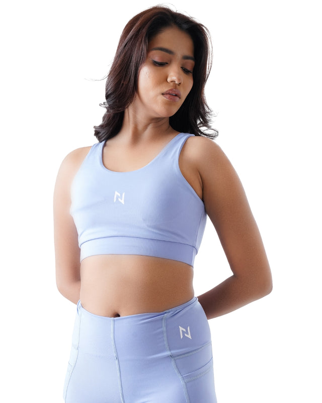 Woman wearing a light blue sports bra and leggings with a logo on a white background
