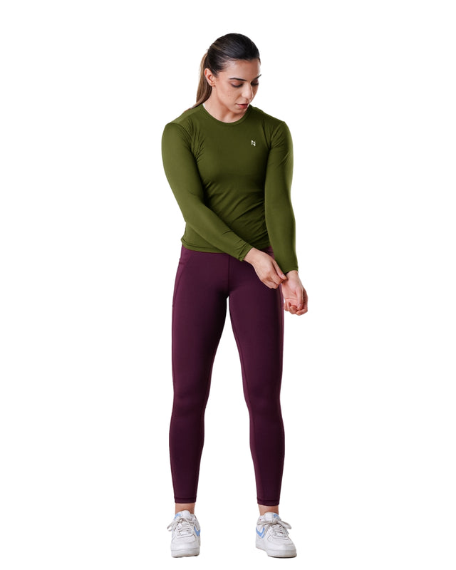 Woman wearing a green long-sleeve top and maroon leggings on a white background