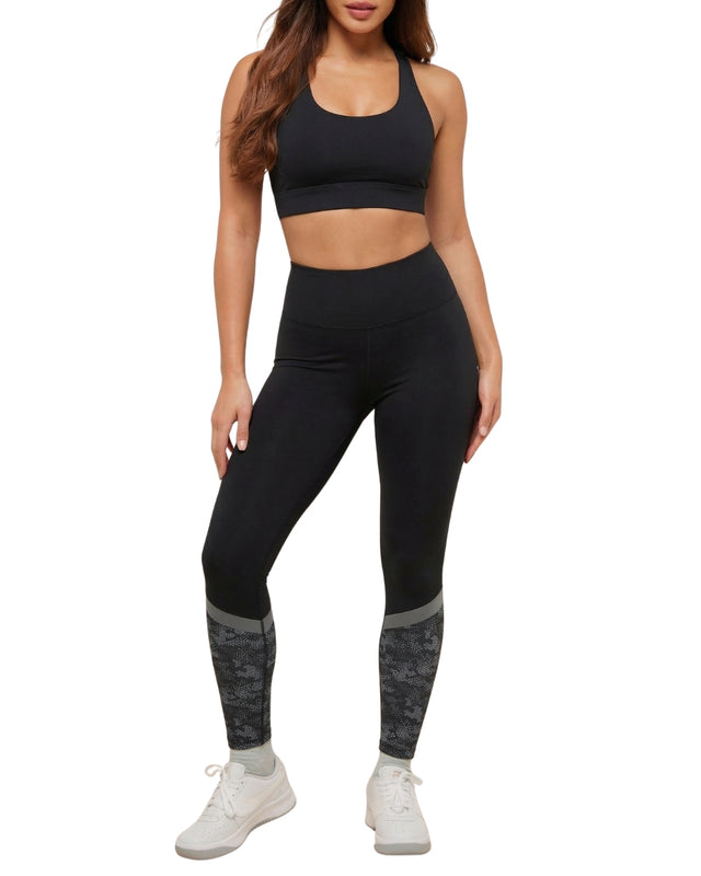 Person wearing a black sports bra and leggings with camouflage accents on a white background