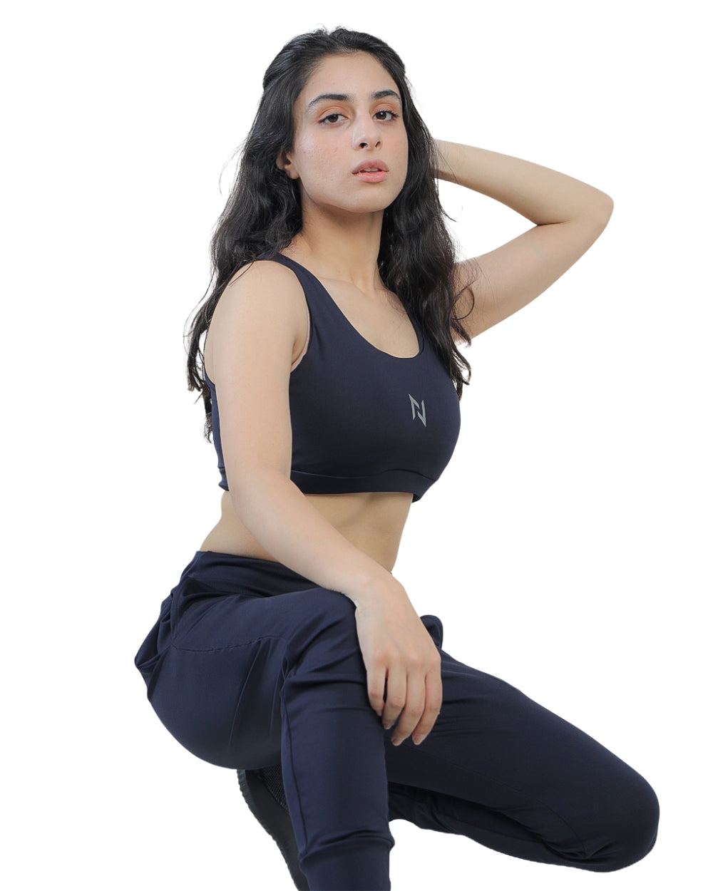 Woman wearing a black sports bra and navy pants on a white background