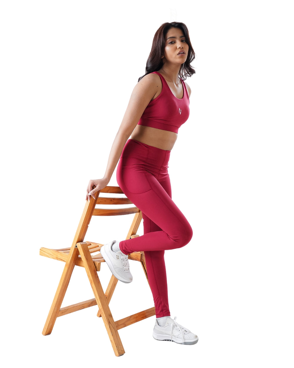 Woman in red athletic wear sitting on a wooden stool against a white background