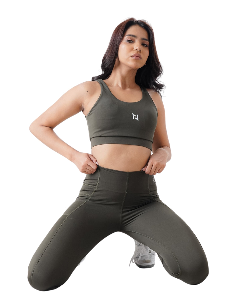 Woman wearing a green sports bra and leggings with a white logo on a white background