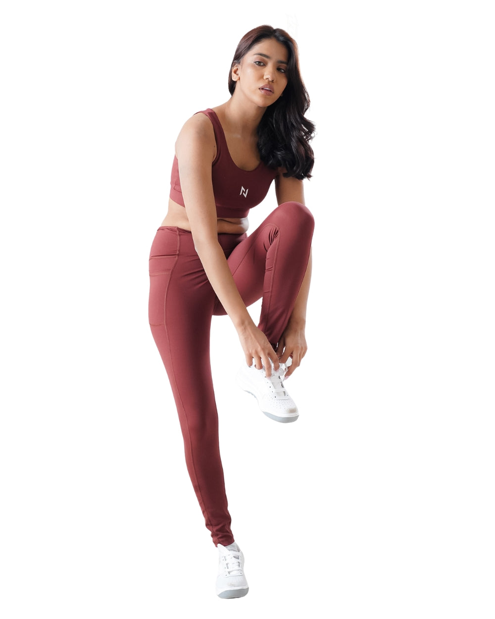 Woman wearing a maroon athletic outfit with white sneakers on a white background