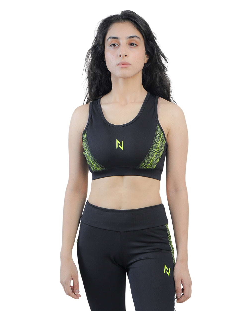 Woman wearing a black sports bra and leggings with green accents on a white background