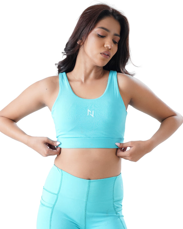 Woman wearing a turquoise sports bra and leggings with a visible brand logo on a white background