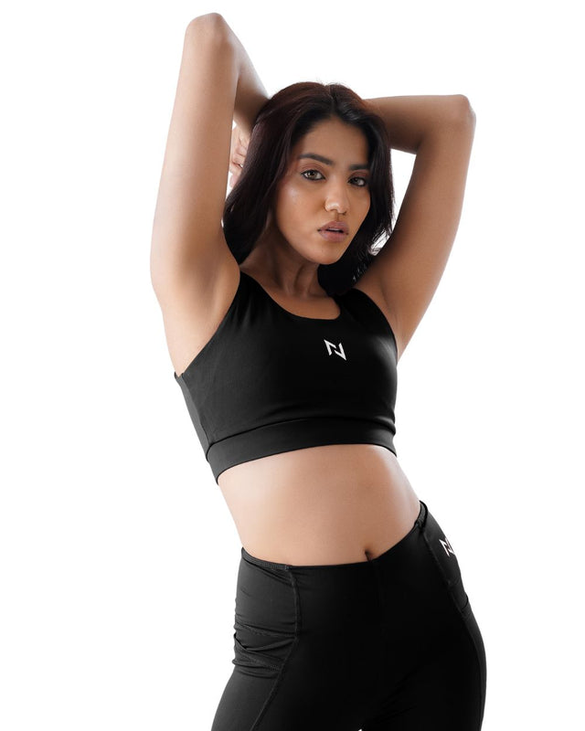 Woman wearing a black sports bra and leggings with a white logo on a white background