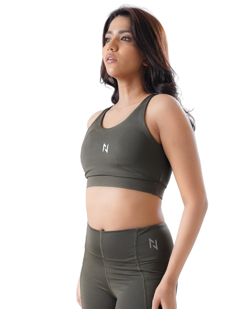 Woman wearing an olive green sports bra and leggings with a brand logo on a white background
