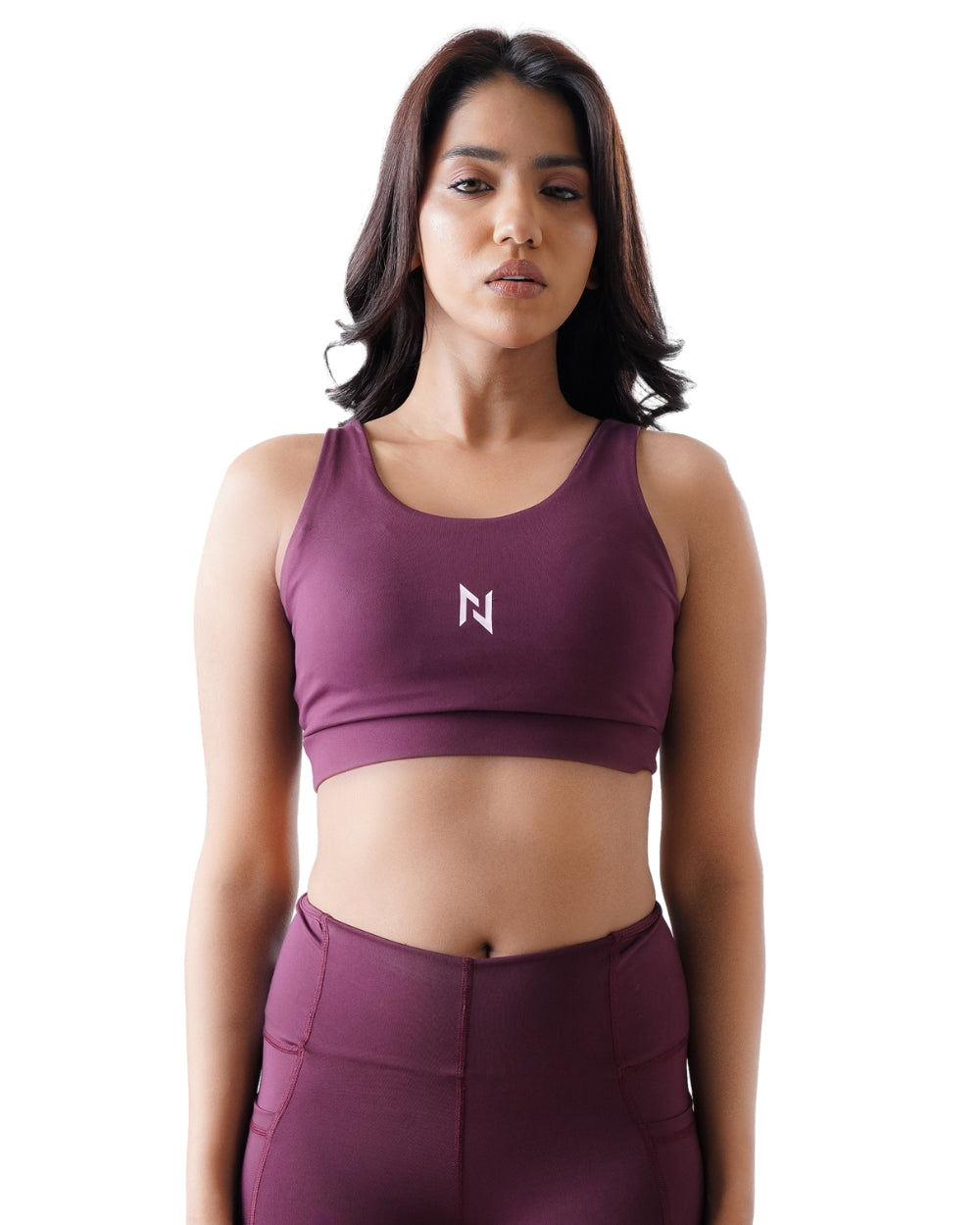 Woman wearing a maroon sports bra and leggings with a logo on a white background