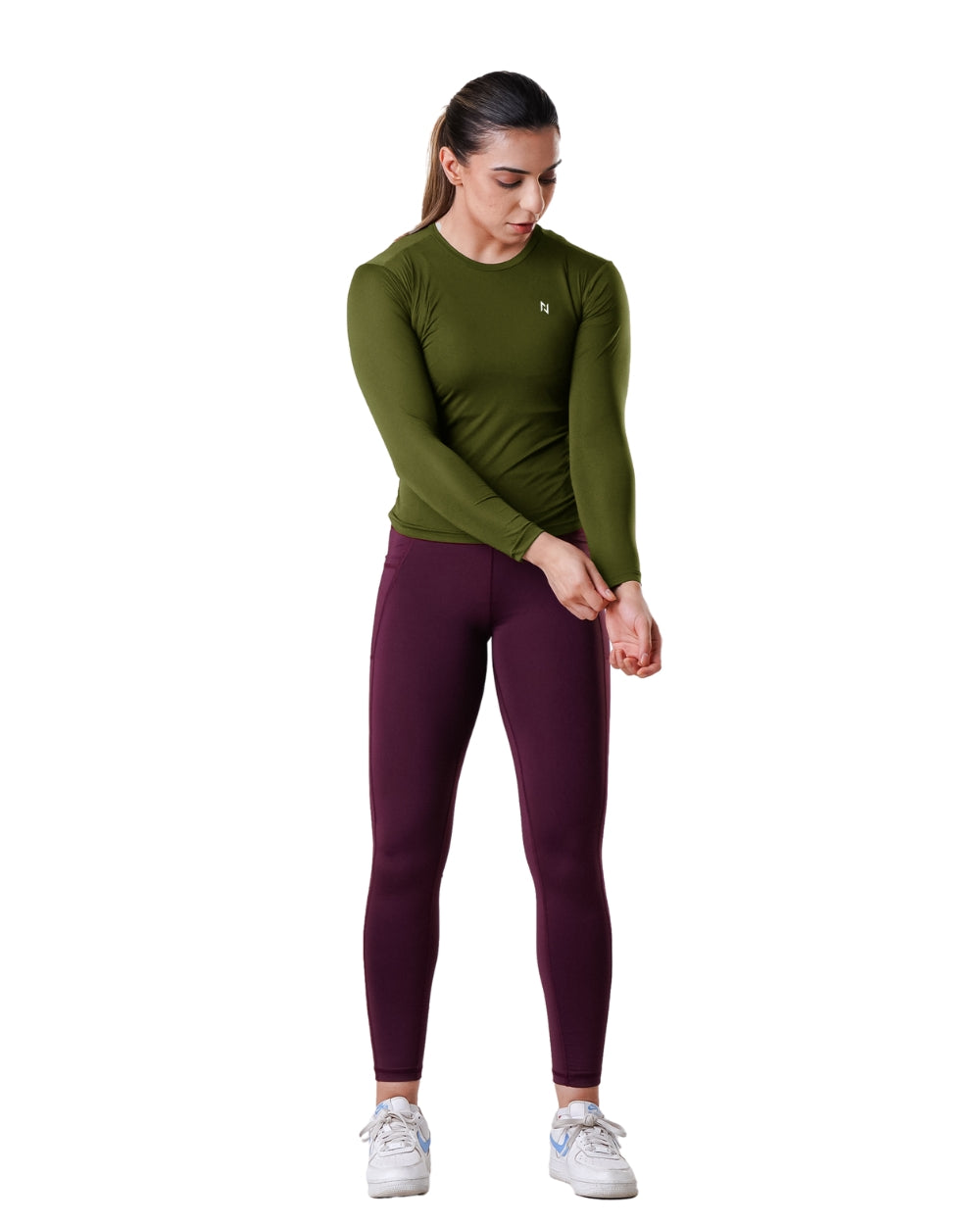 Woman wearing a green long-sleeve top and maroon leggings on a white background
