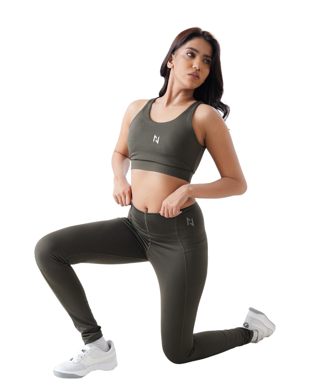 Woman wearing a green sports bra and leggings with a white logo on a white background