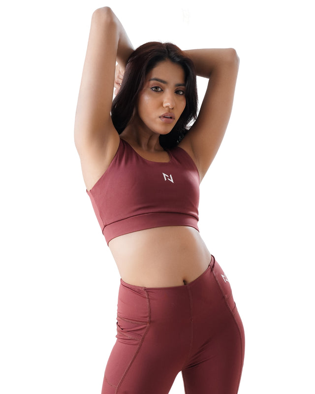 Woman wearing a maroon sports bra and leggings with a logo on a white background